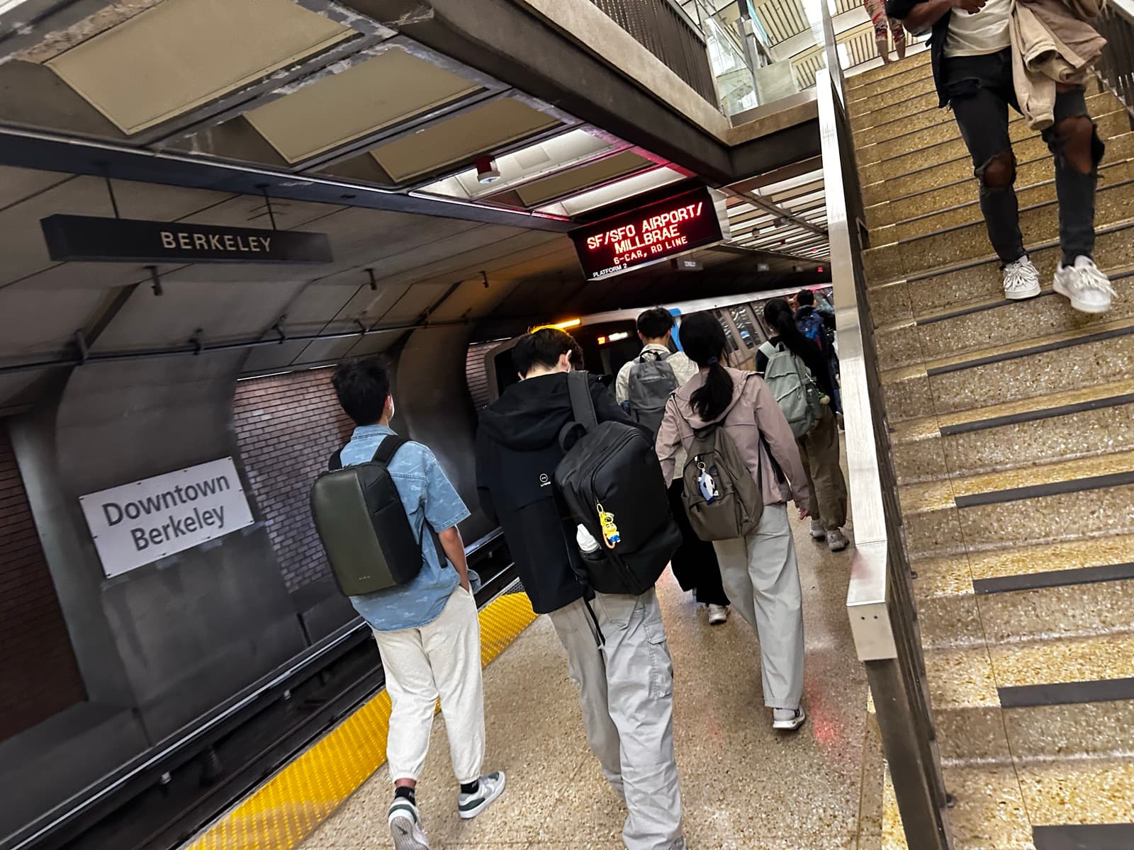 A group of friends with backpacks walking down the Downtown Berkeley BART platform toward the train