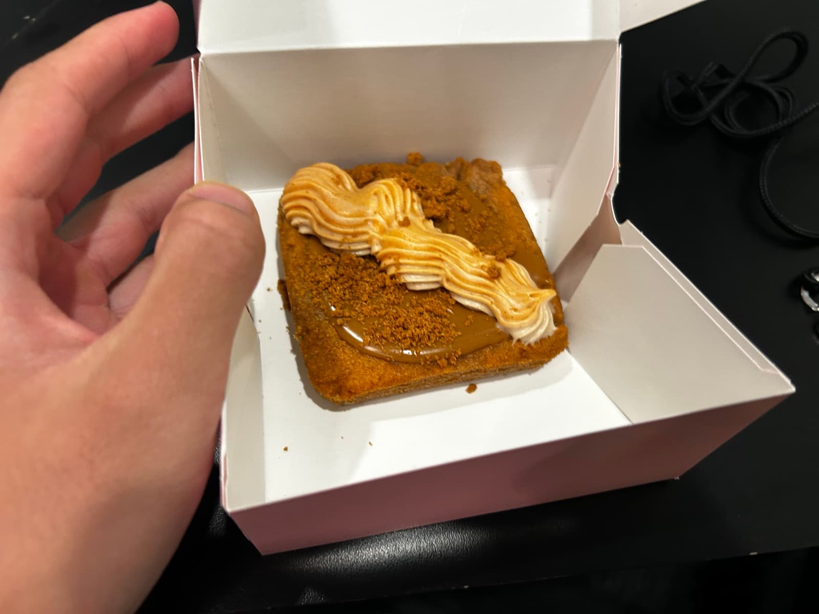 A hand holding a small box with a pastry topped with piped cream and crumbs
