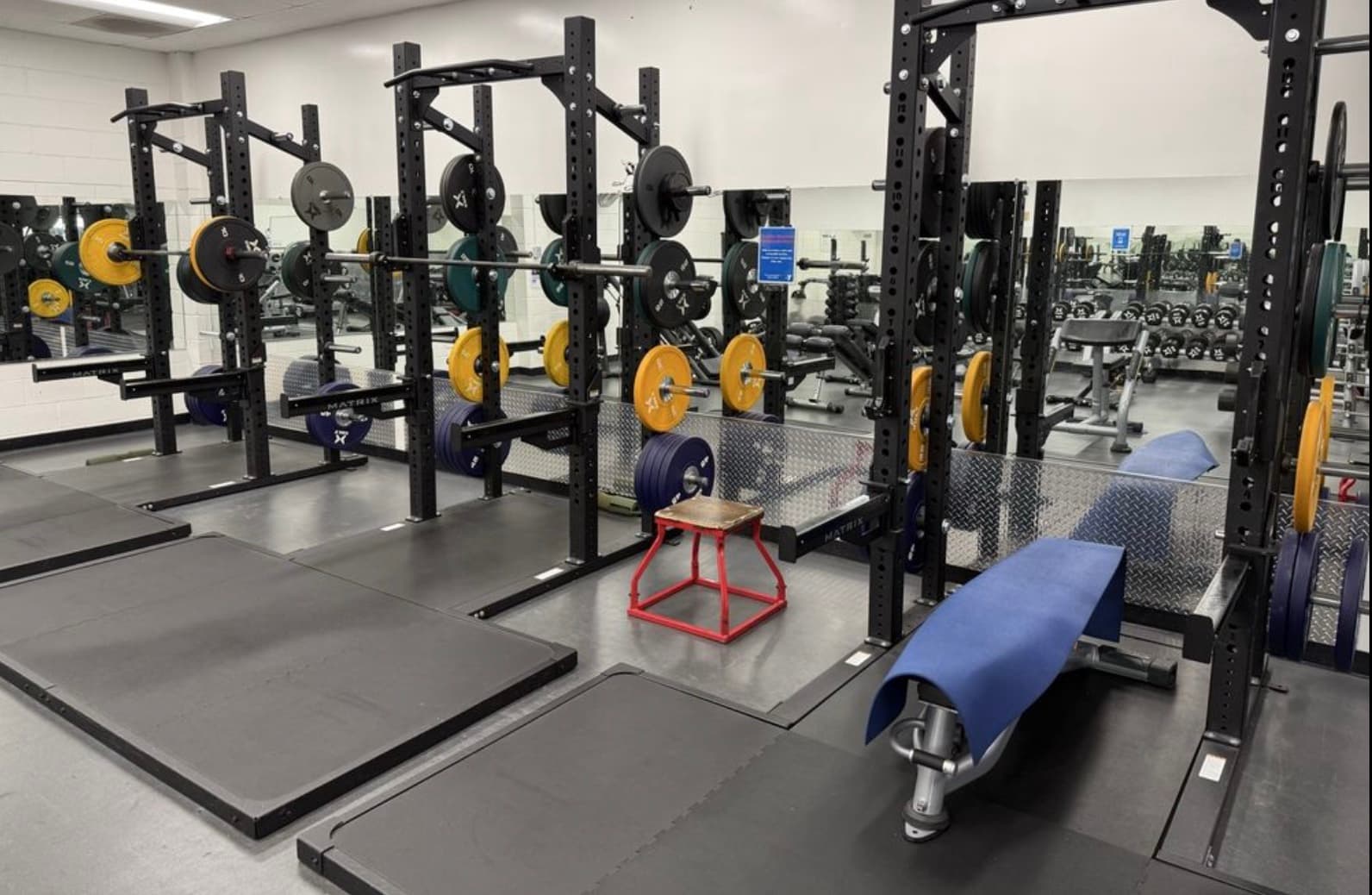 The YMCA weight room: a row of squat racks loaded with bumper plates, lifting platforms, a bench and a plyo box